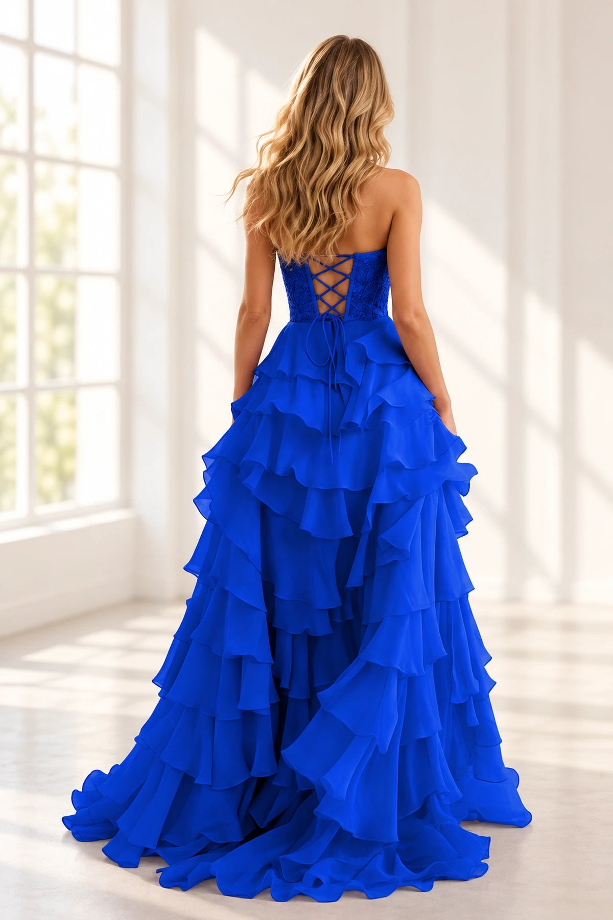 Back view of royal blue prom dress featuring a crisscross lace-up corset, floral lace bodice, long tie ribbons, and voluminous layered ruffle skirt.