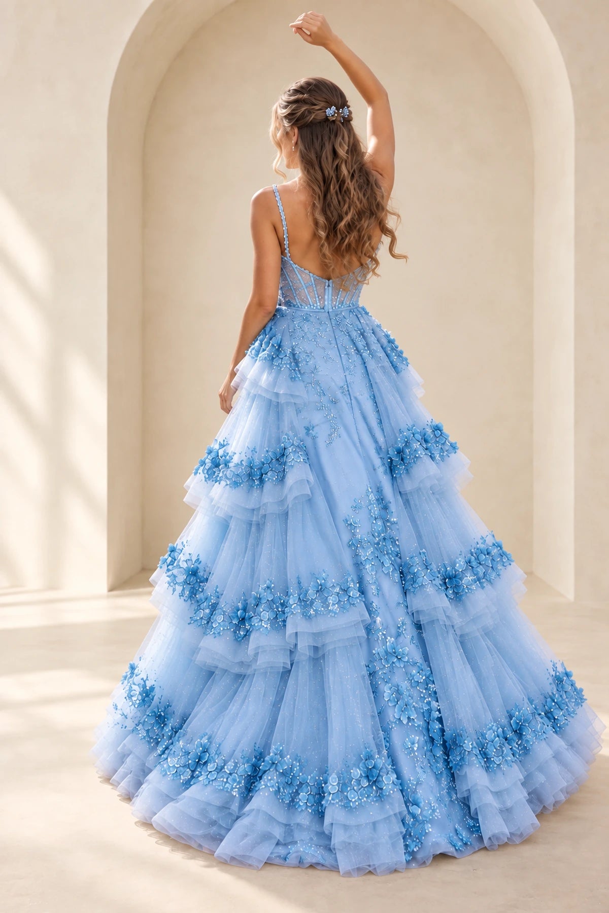 Back view of a light blue 3D floral tulle prom gown with a sheer corset back, delicate spaghetti straps, sparkling floral appliques, and layered ruffled skirt.