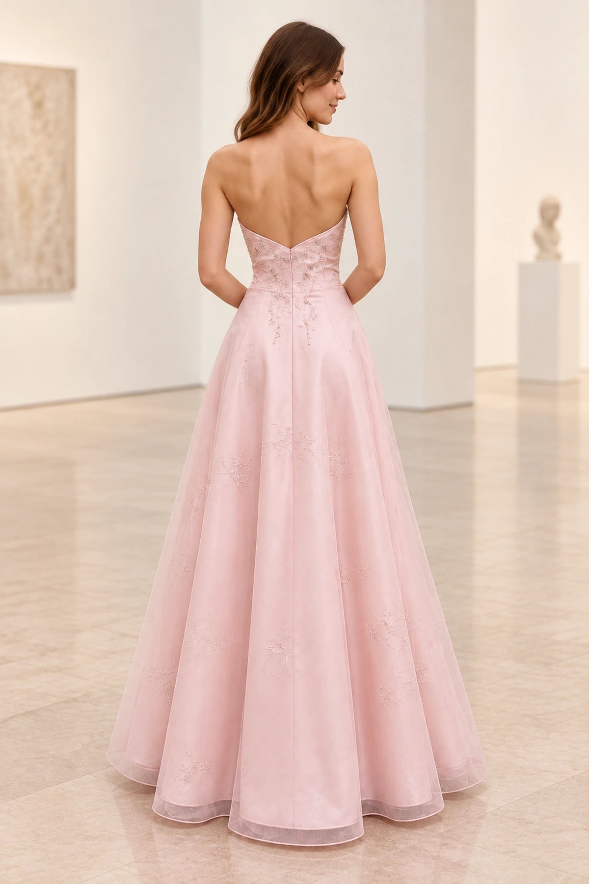 Back view of blush pink satin and tulle prom dress featuring V-shaped strapless back, floral beadwork, fitted waist and flowing A-line skirt