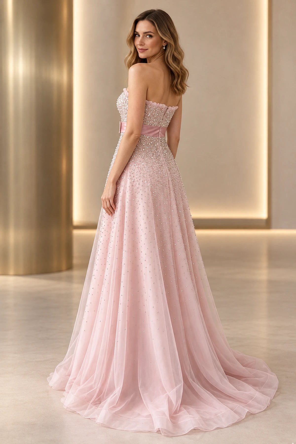 Back view of blush pink beaded tulle prom dress featuring strapless ruffle trim, center back closure, satin waistband and flowing embellished A-line skirt