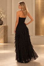 Black prom dress showing a low curved back, center zipper, fitted hips, and long cascading ruffles extending to the floor.