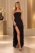 Black strapless sheath prom dress with a straight neckline, fitted waist, cascading asymmetric ruffles, and high front slit.