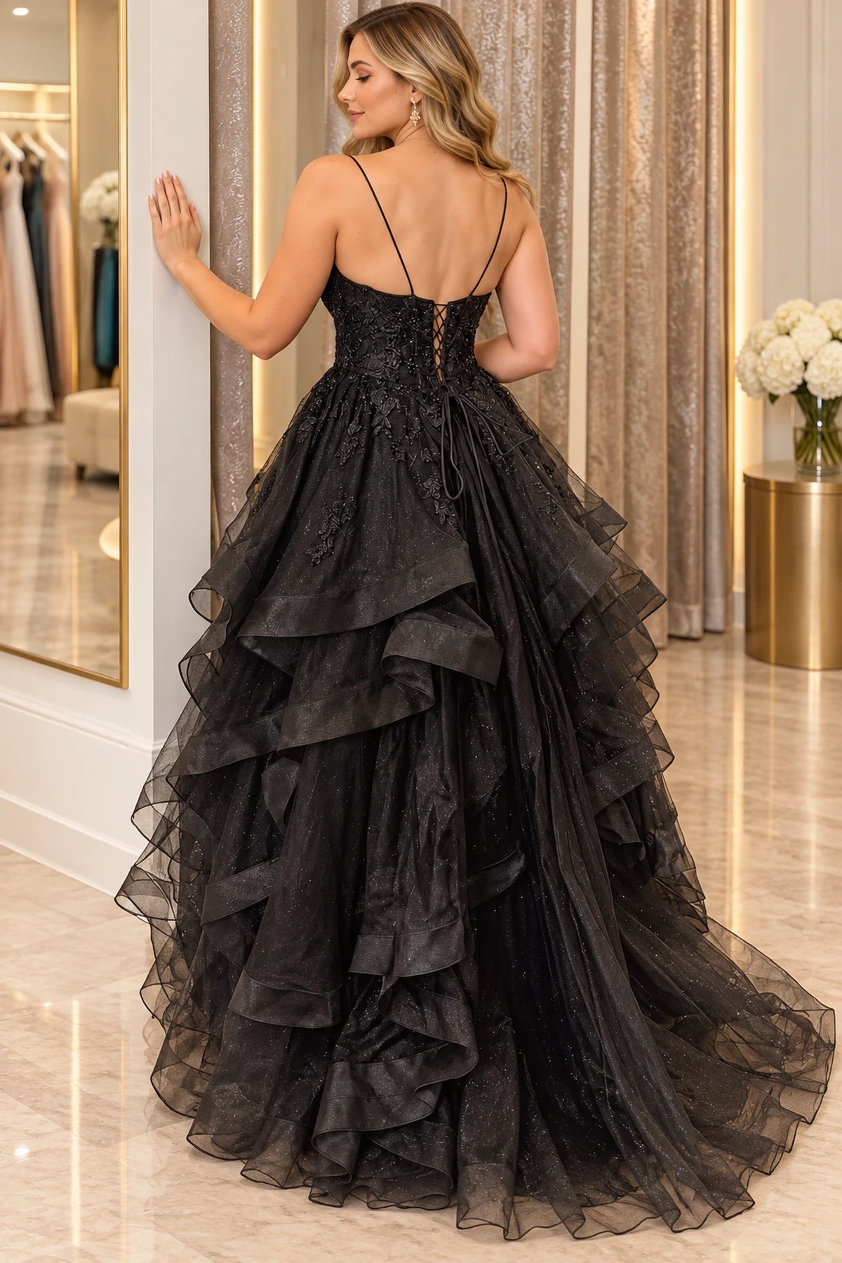 Back view of black ball gown prom dress with thin spaghetti straps, a lace-up corset back, floral lace appliques, and cascading glitter tulle ruffles by Graceprom.