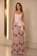 Blush wedding guest dress with strapless corset bodice, floral embroidered floor-length skirt and statement side bow