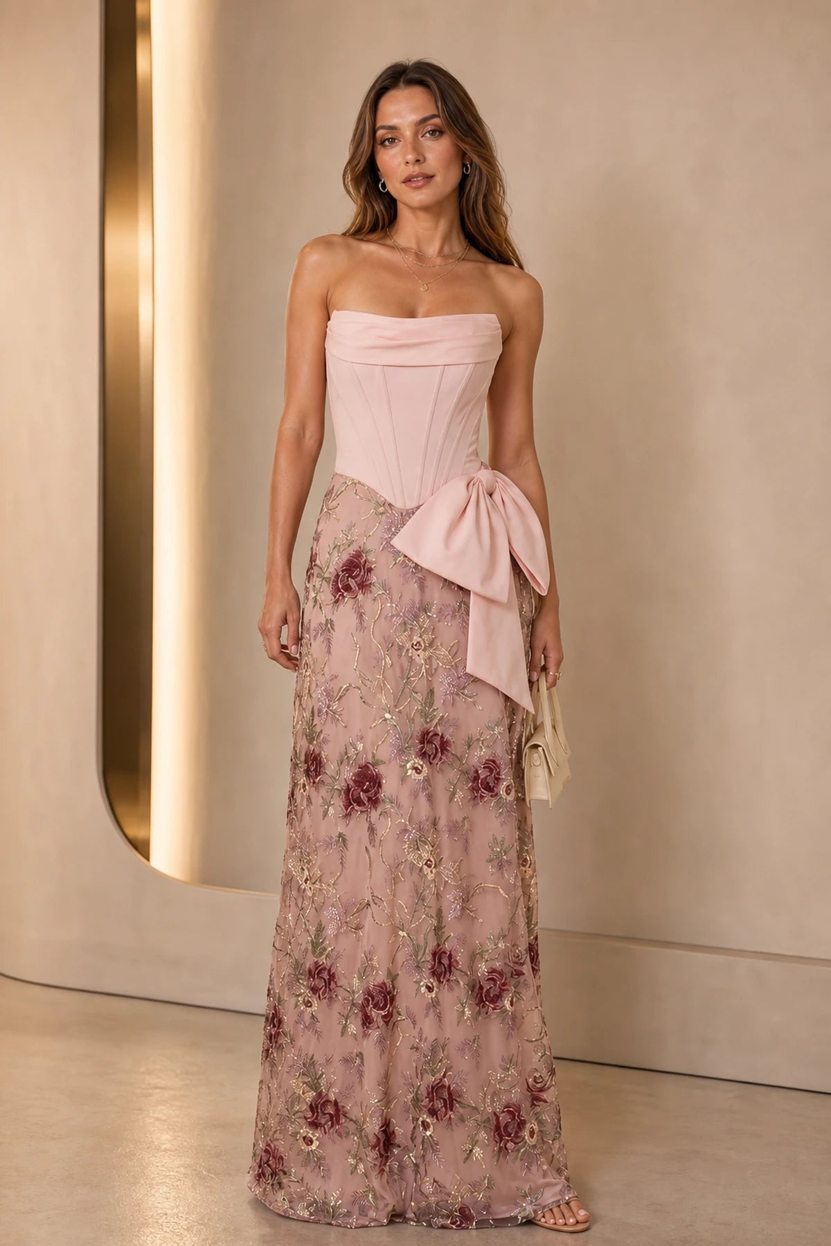 Blush wedding guest dress with strapless corset bodice, floral embroidered floor-length skirt and statement side bow