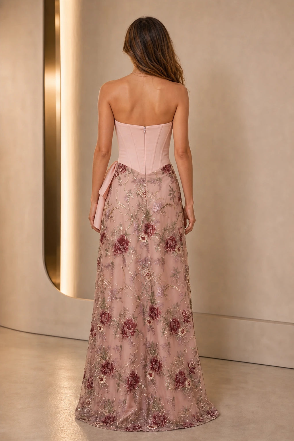 Back view of blush floral wedding guest dress with strapless corset bodice, center zipper and embroidered floor-length skirt