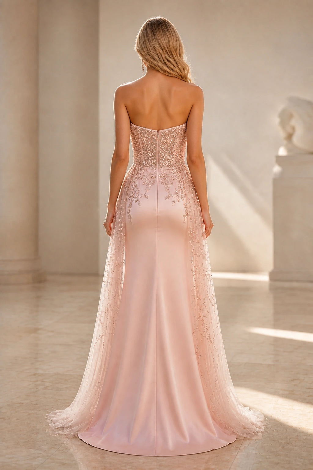 Back view of blush pink wedding guest dress with strapless zipper back, beaded detailing and floor-length sheer overlay