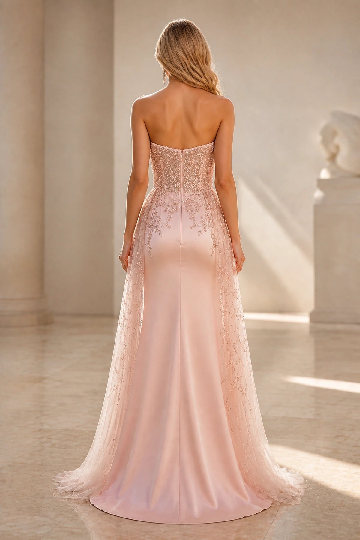 Back view of blush pink wedding guest dress with strapless zipper back, beaded detailing and floor-length sheer overlay
