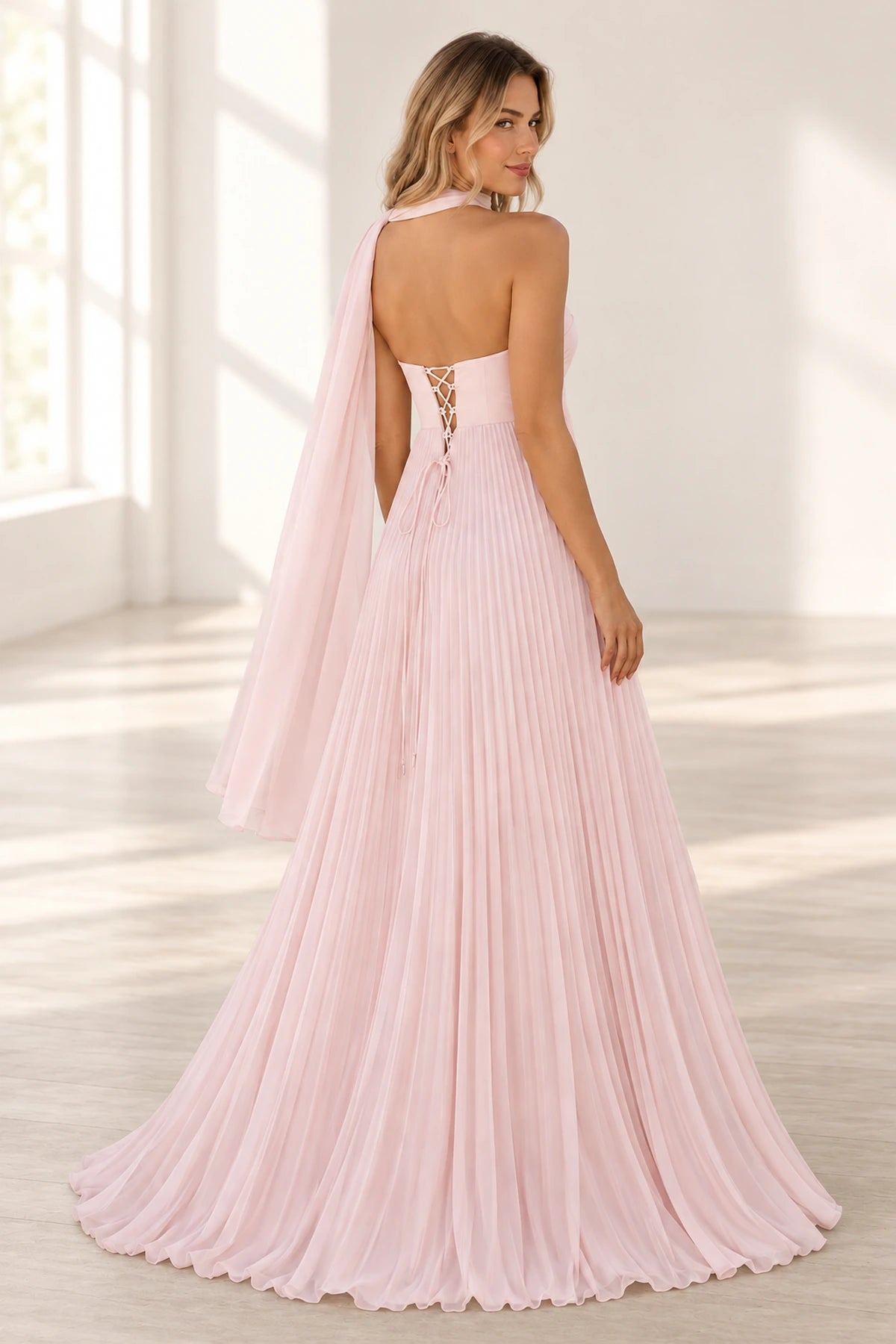 Back view of blush pink chiffon prom dress featuring an open upper back, crisscross lace-up closure, flowing neck scarf, and floor-length pleated A-line skirt.