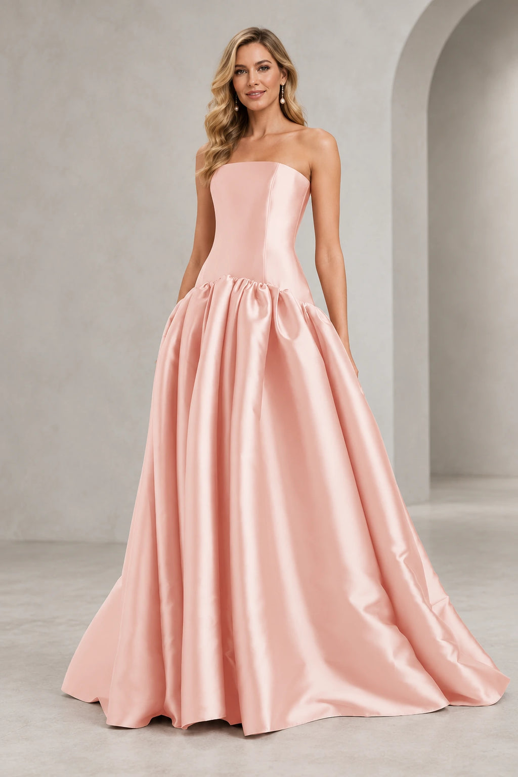 Blush pink strapless A line prom dress with a straight neckline, elongated fitted bodice, curved drop waist, and full gathered floor-length skirt.