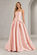 Blush pink strapless A line prom dress with a straight neckline, elongated fitted bodice, curved drop waist, and full gathered floor-length skirt.