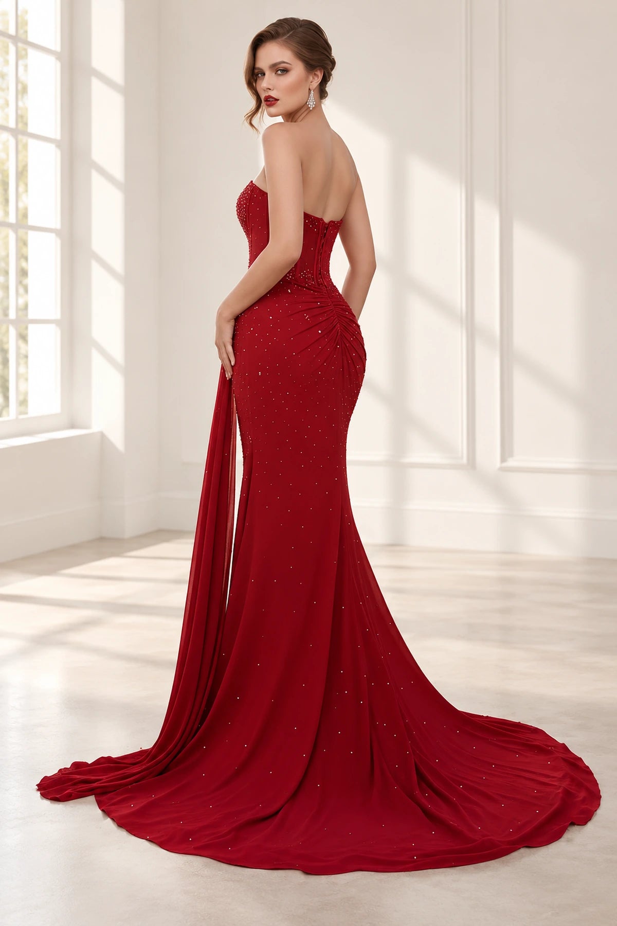 Back view of burgundy mermaid prom dress featuring a fitted zipper-back corset, ruched hip detailing, sparkling embellishments and sweeping train.
