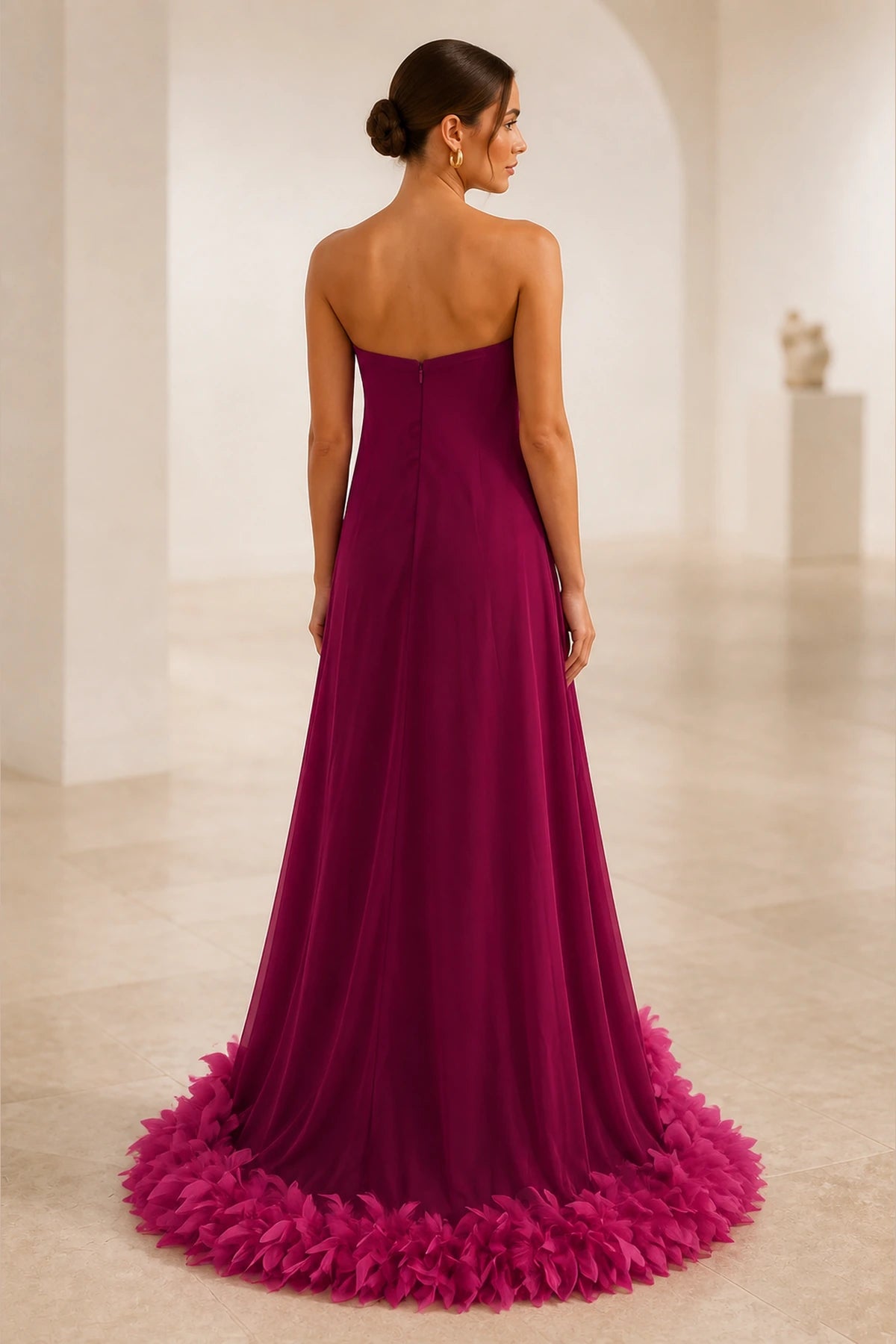 Back view of burgundy wedding guest dress with strapless low back, center zipper and dramatic fuchsia feather-style hem