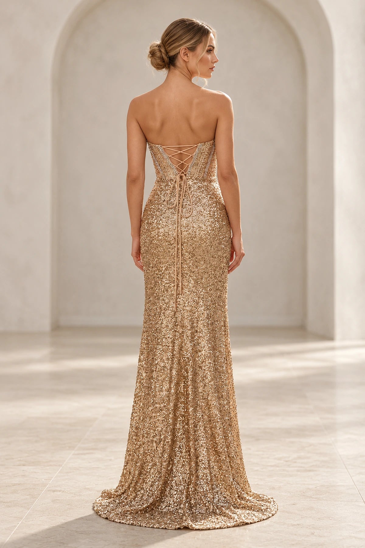 Back view of champagne gold mermaid prom dress featuring a crisscross lace-up corset closure, intricate shimmering embellishments, and a subtle sweep train.