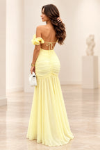 Back view of yellow satin A-line prom dress featuring ruffle shoulder straps, open back with large bow tie and flowing pleated floor length skirt