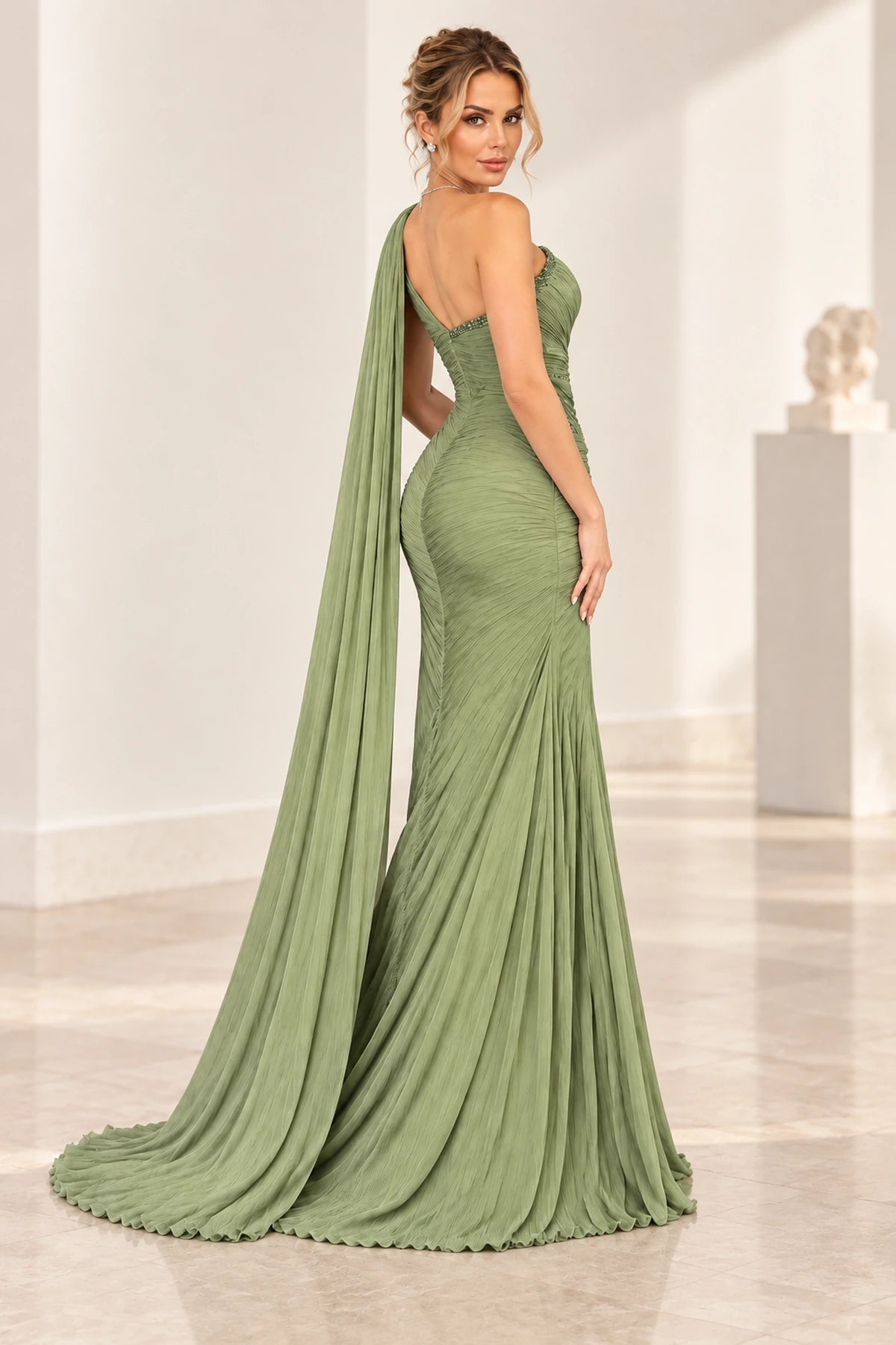 Back view of Graceprom sage green chiffon wedding guest dress with a beaded asymmetric low back, ruched hips and a long trailing shoulder cape.