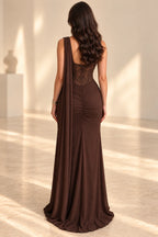 Back view of a chocolate brown chiffon evening gown with a sheer beaded corset back, visible boning, ruched fitted skirt, and long flowing shoulder cape.
