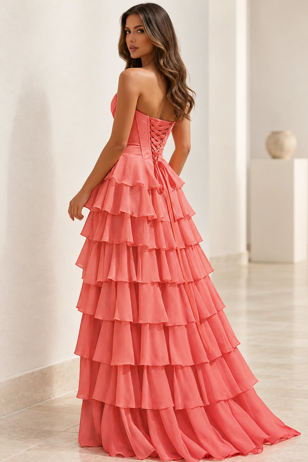 Back view of coral pink strapless prom dress featuring a crisscross lace-up corset closure, fitted waist, and cascading tiered ruffle skirt.