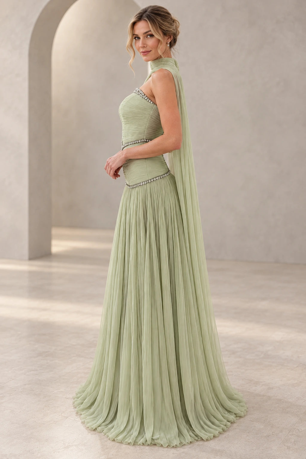 Sage green chiffon A-line prom dress with a strapless beaded neckline, ruched fitted bodice, flowing cape back and floor-length pleated skirt, side view