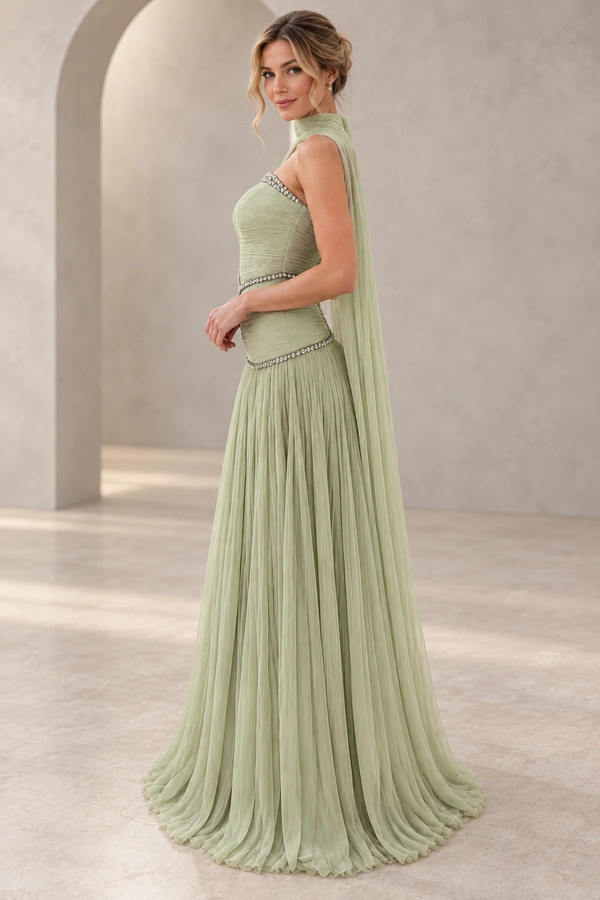 Sage green chiffon A-line prom dress with a strapless beaded neckline, ruched fitted bodice, flowing cape back and floor-length pleated skirt, side view