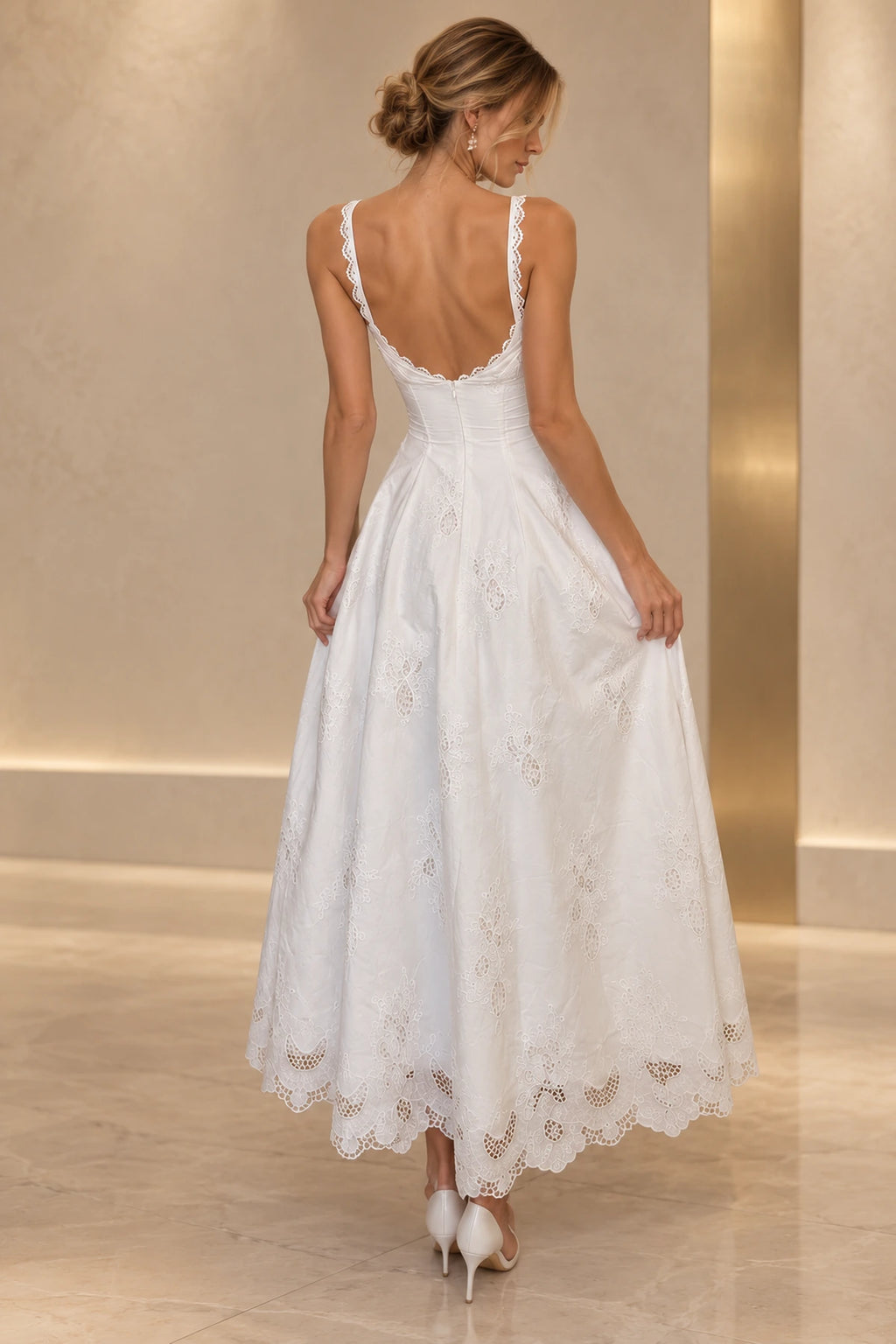 Back view of white embroidered lace wedding guest dress featuring low V back, lace trimmed straps, fitted waist and scalloped tea length A-line skirt