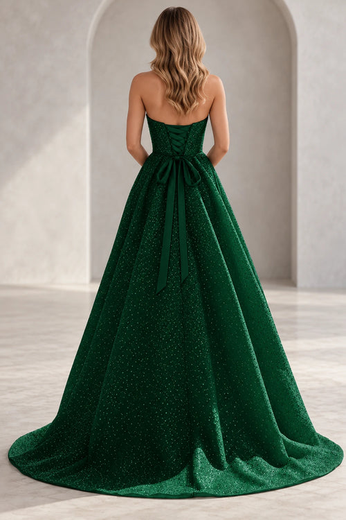 Back view of an emerald green prom dress with corset lacing, a large waist bow, long ribbon tails, and a sparkling skirt with train.
