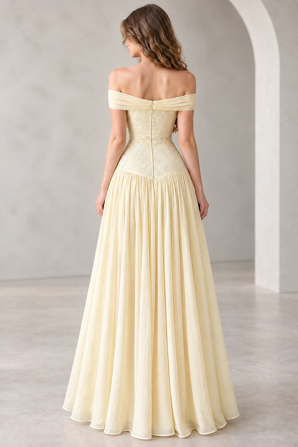 Back view of a light yellow chiffon prom gown featuring an off-the-shoulder draped neckline, floral embroidered fitted bodice, center-back zipper, and flowing A-line skirt.
