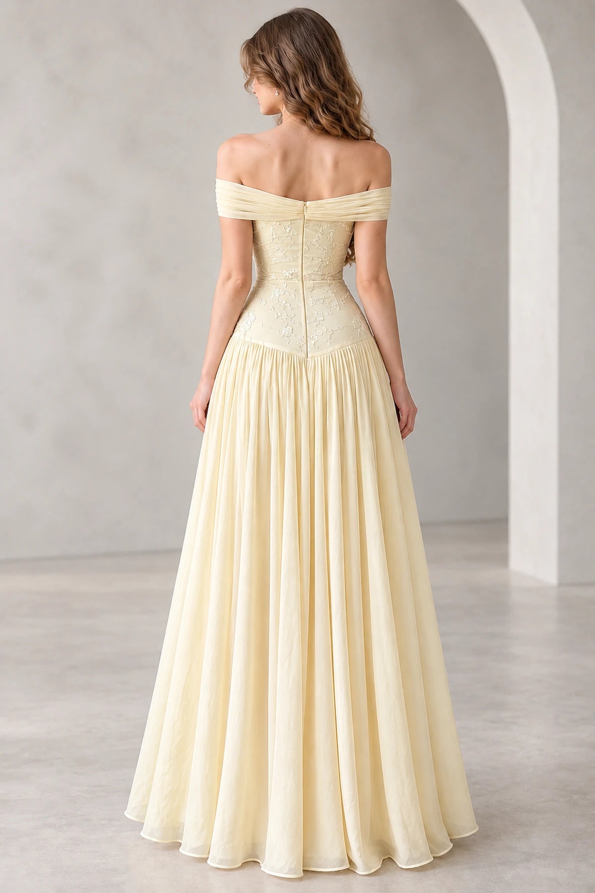 Back view of a light yellow chiffon prom gown featuring an off-the-shoulder draped neckline, floral embroidered fitted bodice, center-back zipper, and flowing A-line skirt.
