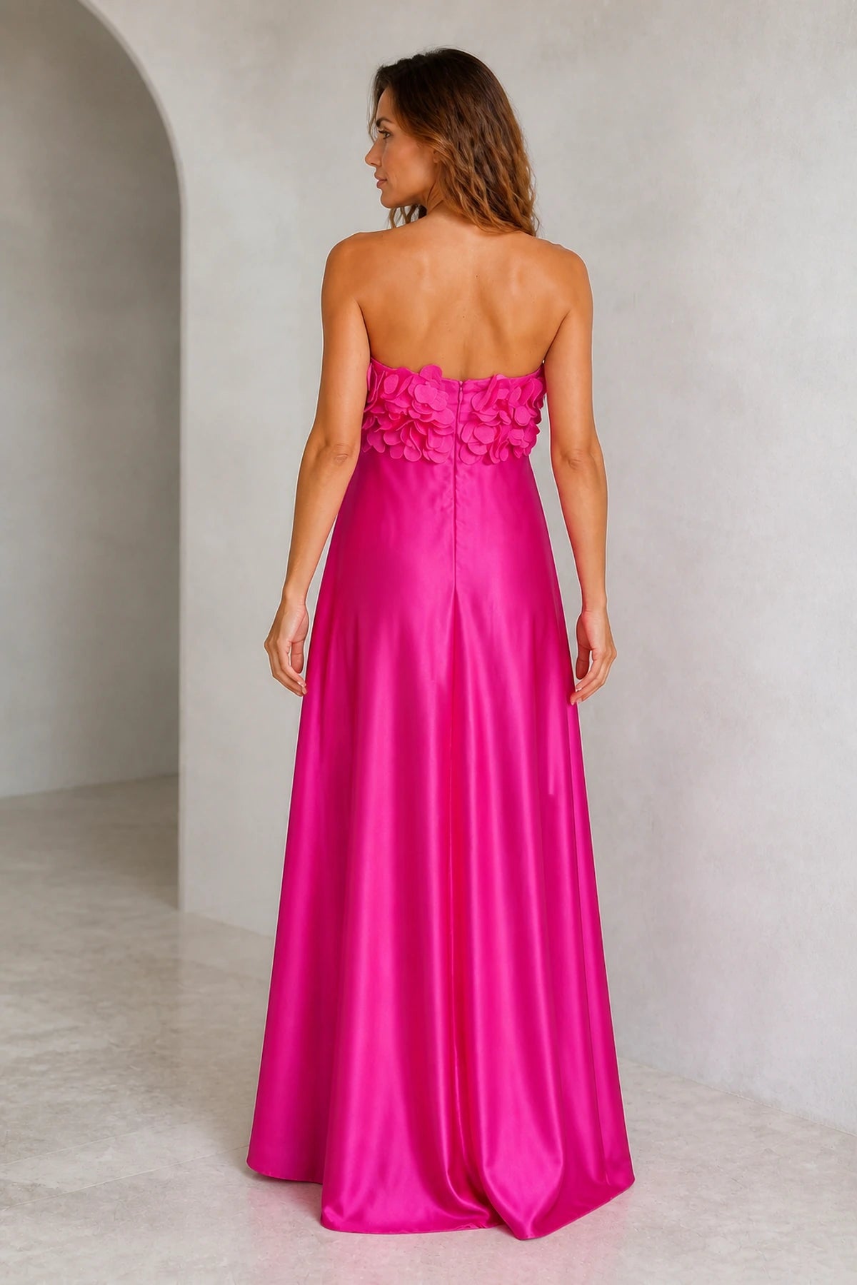 Back view of fuchsia wedding guest dress with strapless open back, 3D floral trim and flowing floor-length A-line skirt