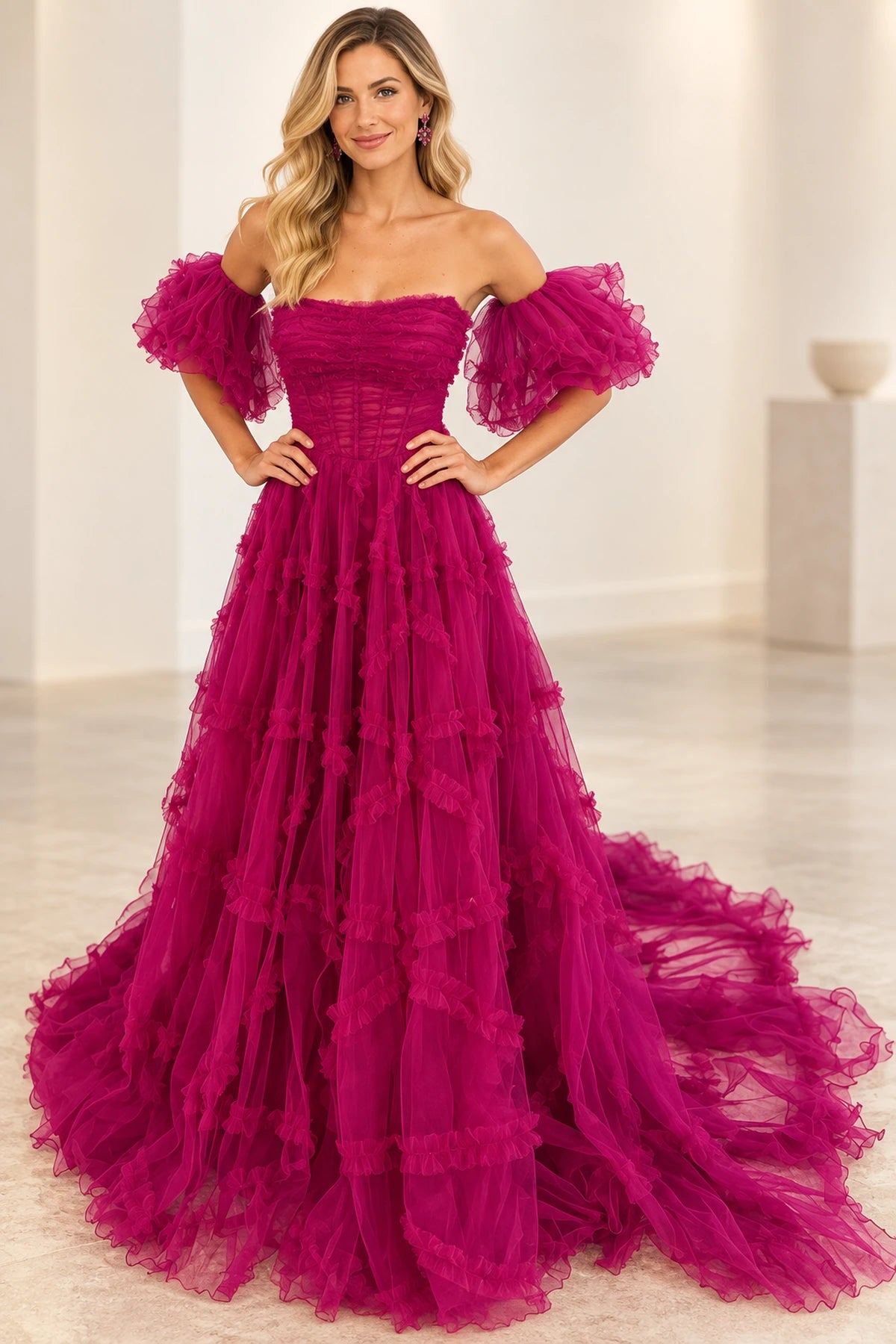 Fuchsia pink ball gown prom dress styled with voluminous off-the-shoulder tulle puff sleeves, a ruched corset bodice, and ruffled tulle skirt by Graceprom.
