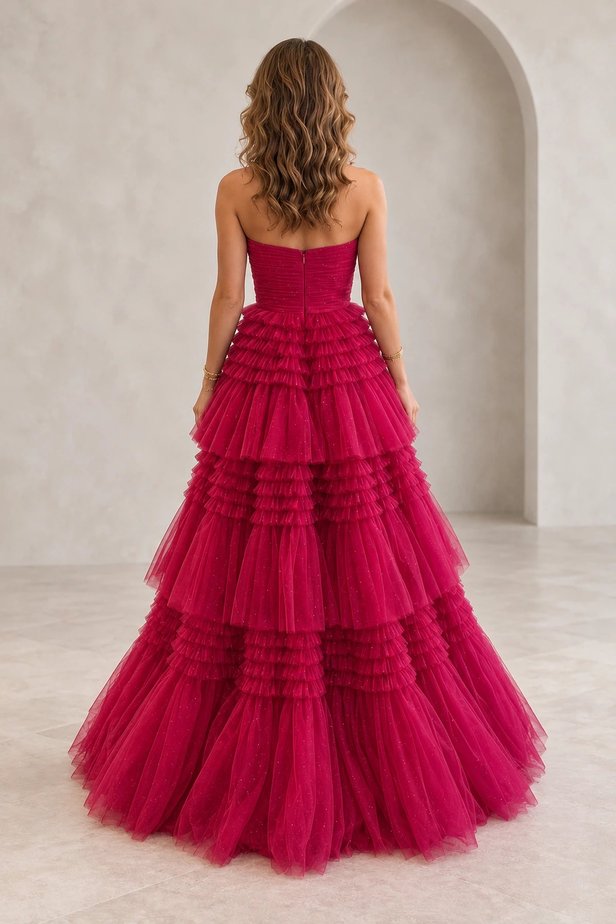 Back view of hot pink glitter tulle prom dress featuring strapless ruched bodice, center back zipper and cascading tiered ruffle A-line skirt