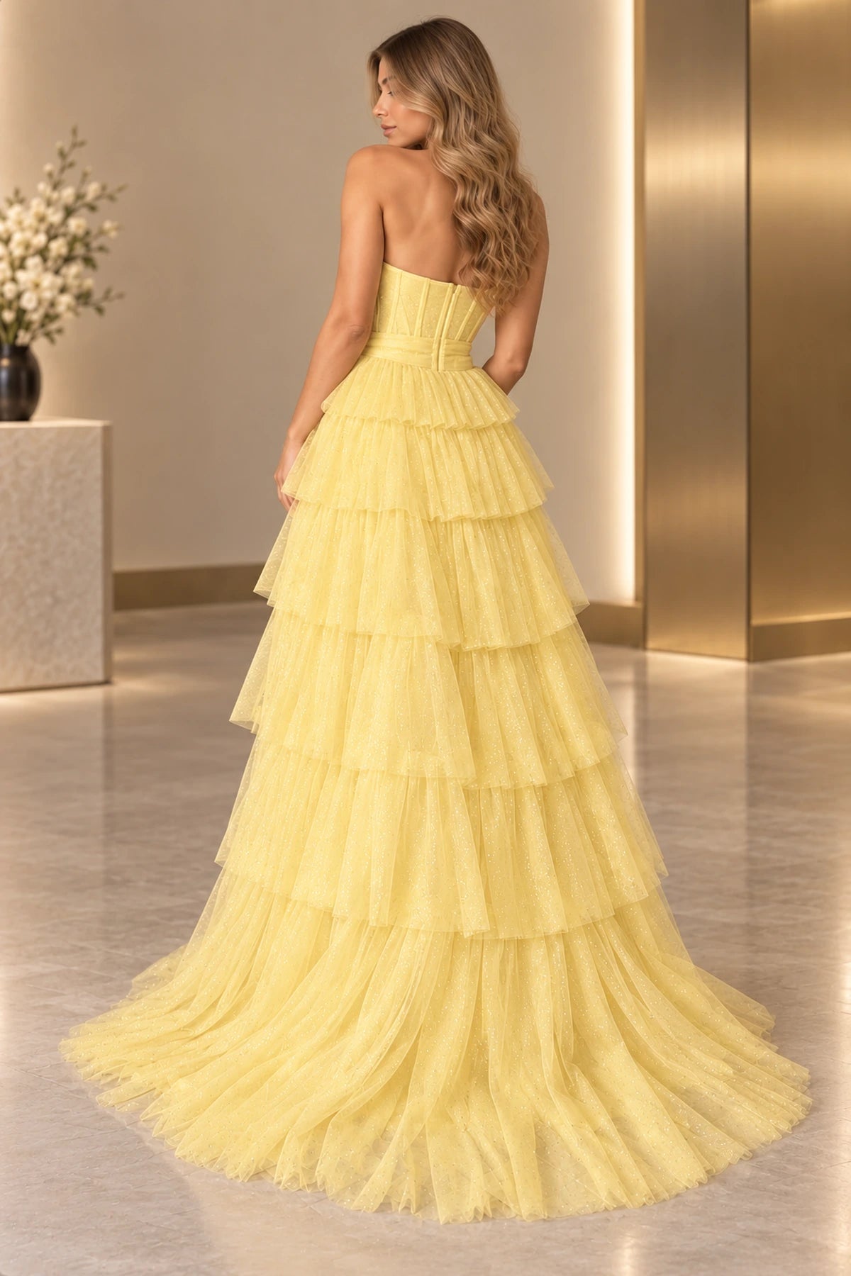 Back view of yellow glitter tulle prom dress featuring strapless corset bodice, fitted waistband, cascading tiered ruffles and floor length sweeping train