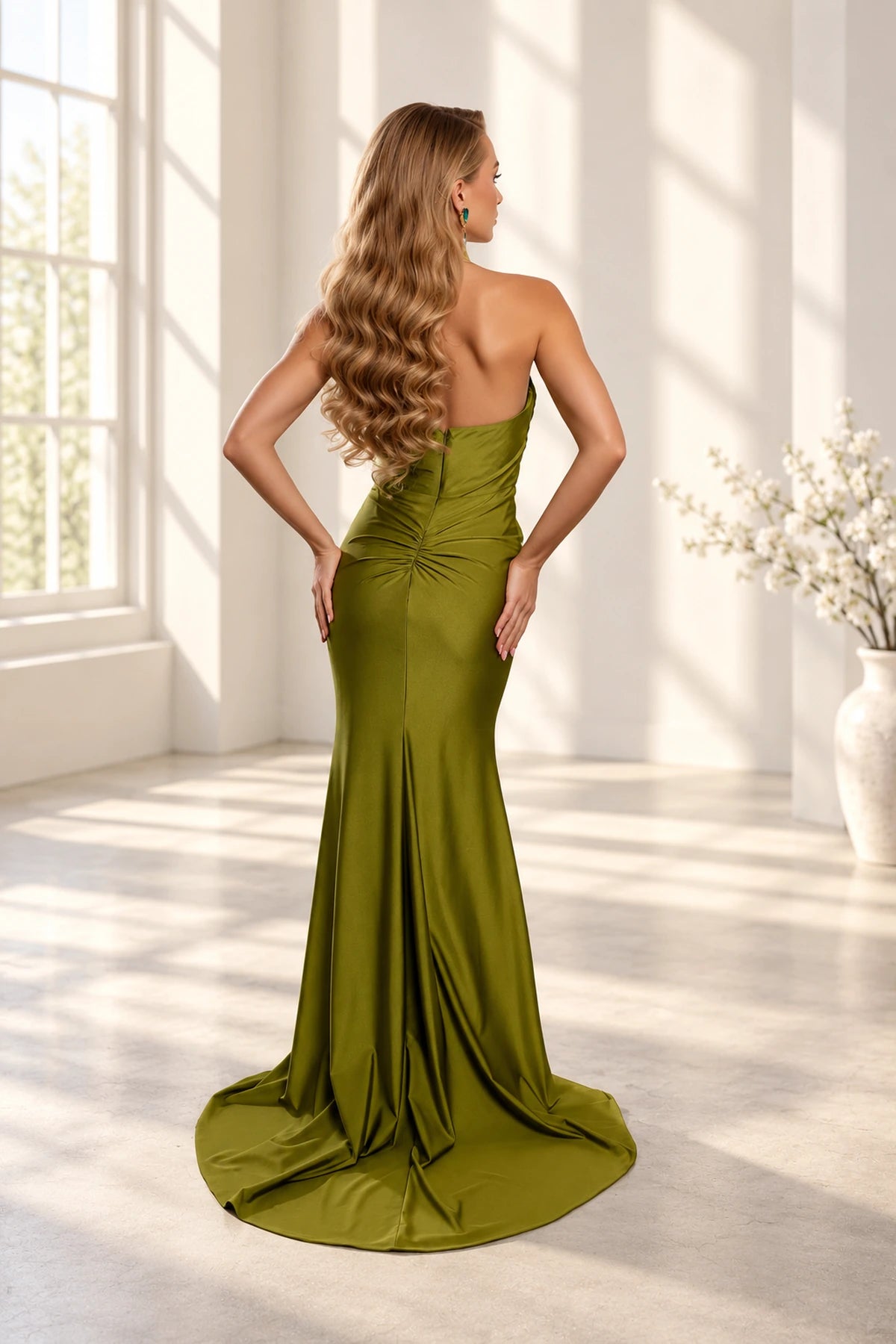 Back view of an olive green prom dress with a low curved neckline, center-back zipper, gathered hip detailing, and sweeping train.