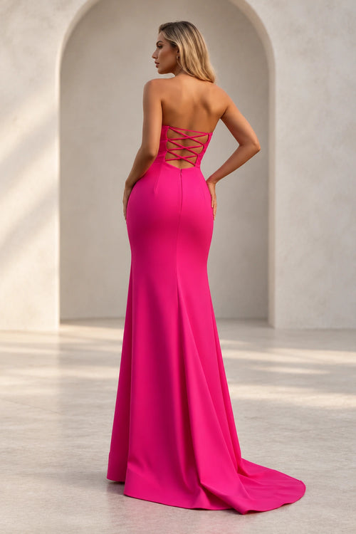 Hot pink mermaid prom dress showing an open back with thin crisscross straps, a center zipper, fitted hips, and a sweeping train.