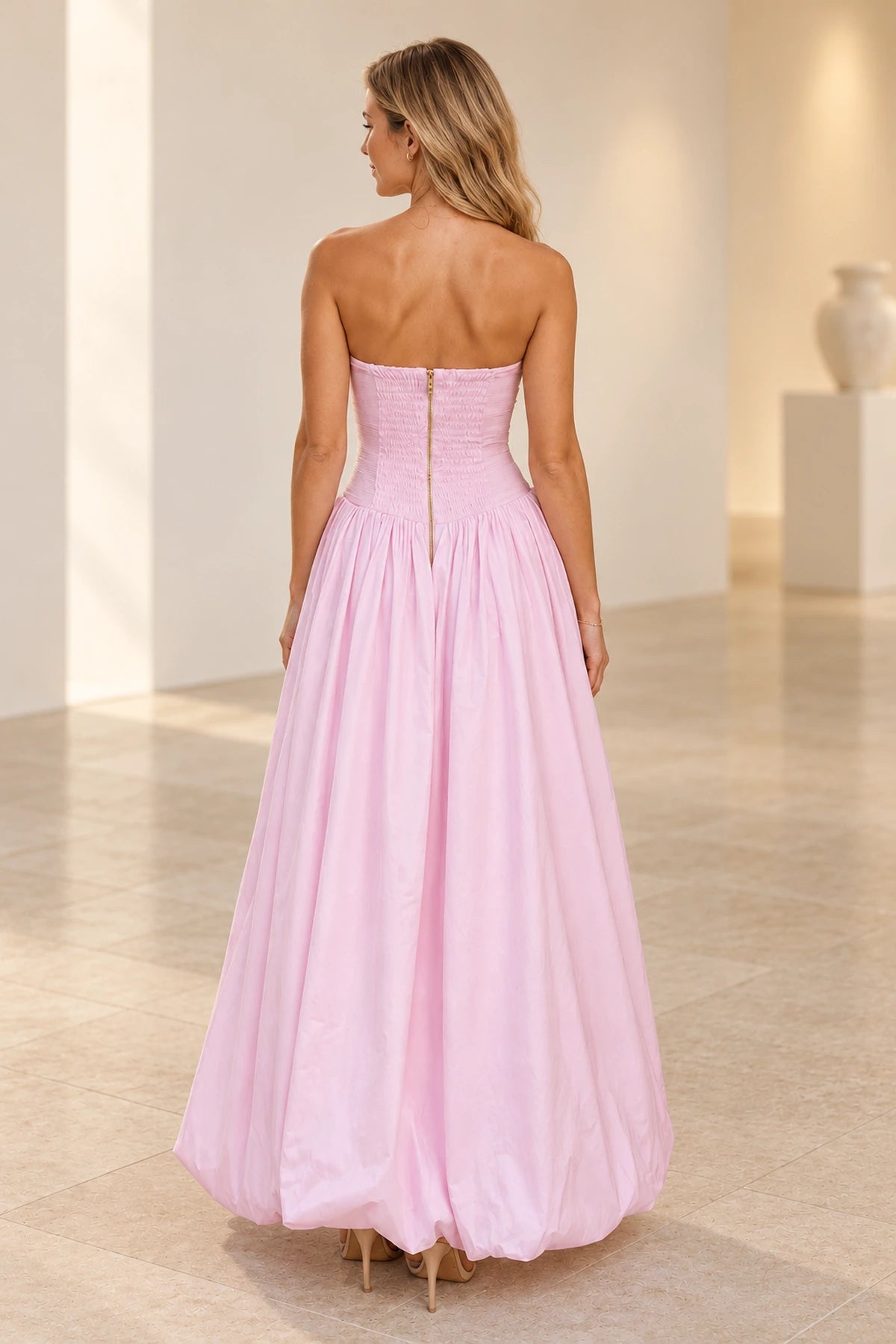 Back view of light pink strapless A-line prom dress featuring a ruched bodice, center zipper closure and full gathered floor-length skirt