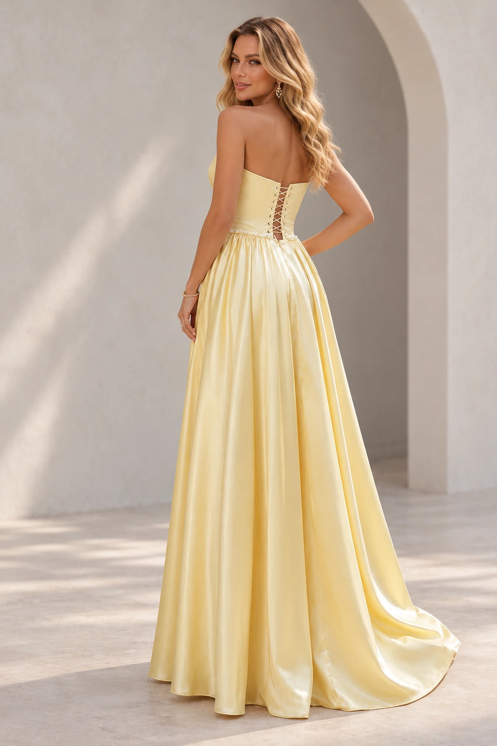 Light yellow prom dress showing a low crisscross lace-up back, pearl-like waist trim, and a full gathered skirt with a trailing hem.