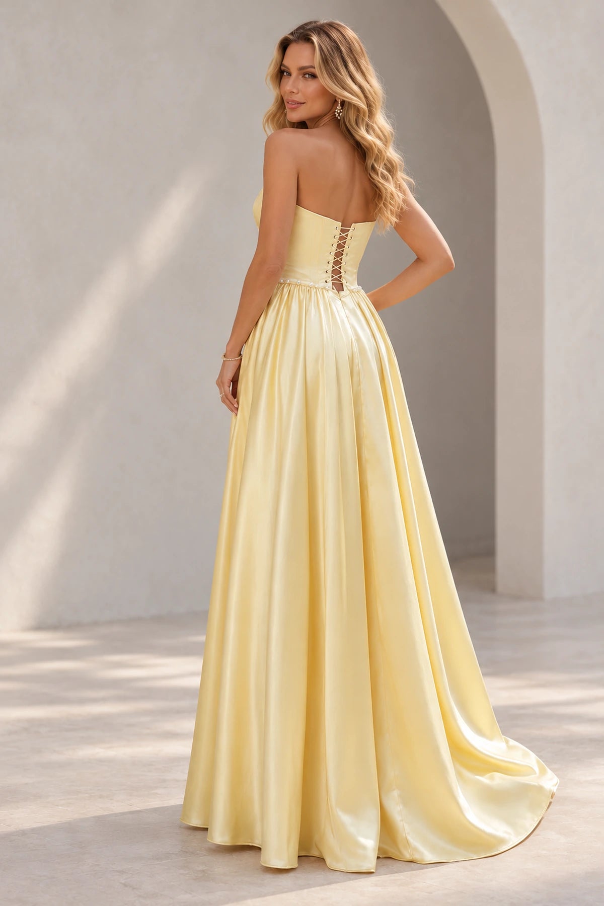 Light yellow prom dress showing a low crisscross lace-up back, pearl-like waist trim, and a full gathered skirt with a trailing hem.