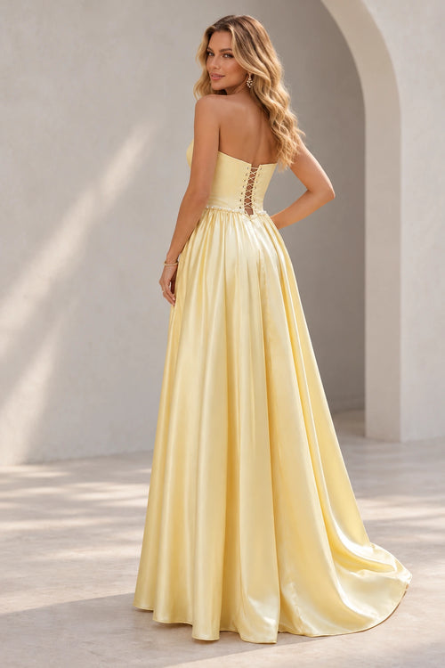Light yellow prom dress showing a low crisscross lace-up back, pearl-like waist trim, and a full gathered skirt with a trailing hem.