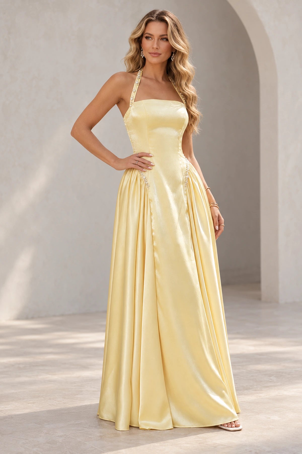 Light yellow A line prom dress with pearl-like halter strap details, a straight neckline, elongated bodice, and gathered side skirt panels.