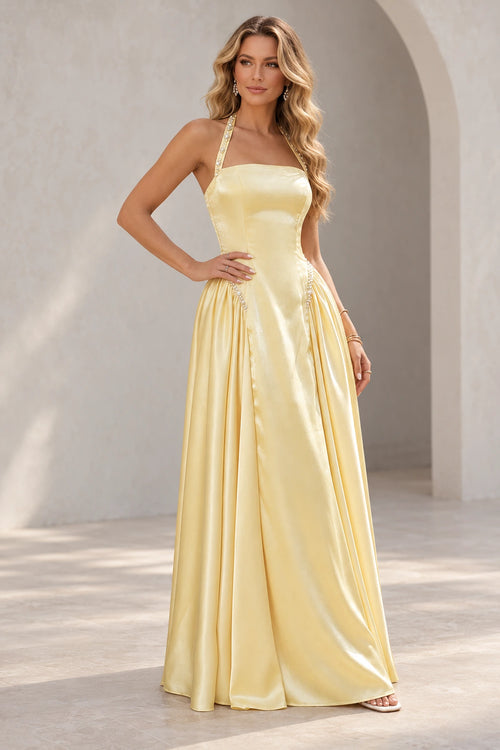 Light yellow A line prom dress with pearl-like halter strap details, a straight neckline, elongated bodice, and gathered side skirt panels.