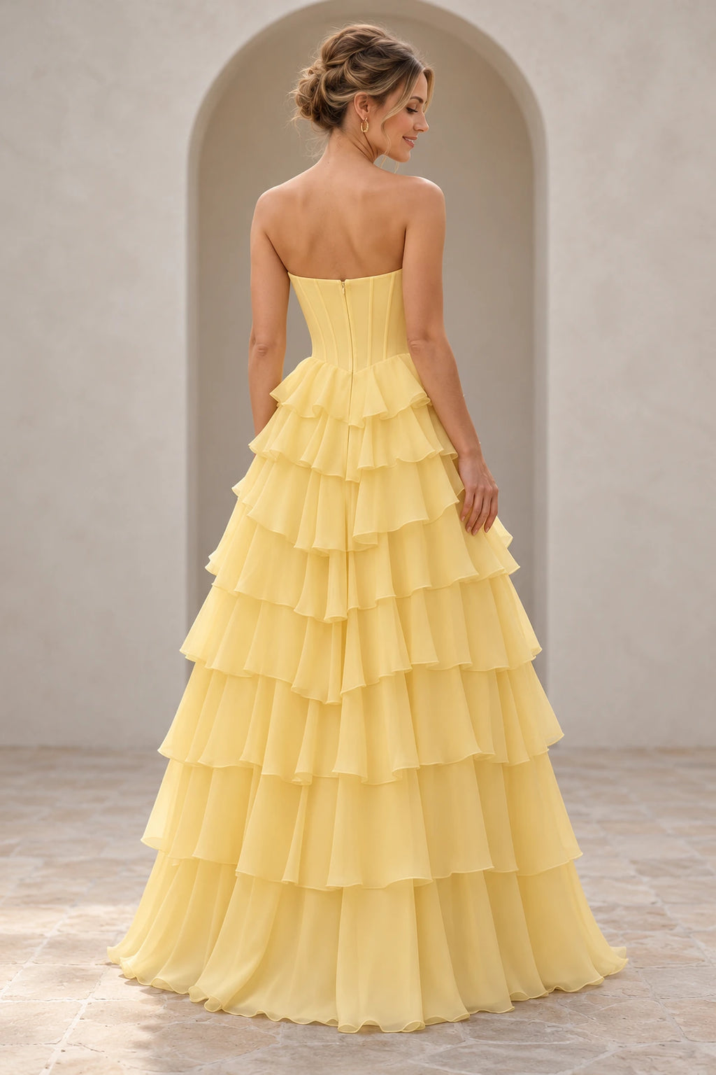 Light yellow prom dress showing a low curved back, vertical bodice panels, center zipper, and cascading floor-length ruffle tiers.