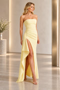 Light yellow strapless sheath prom dress with a straight neckline, pleated bodice, diagonal waist draping, high slit, and cascading side flounce.