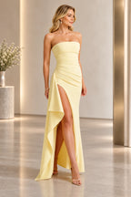 Light yellow strapless sheath prom dress with a straight neckline, pleated bodice, diagonal waist draping, high slit, and cascading side flounce.