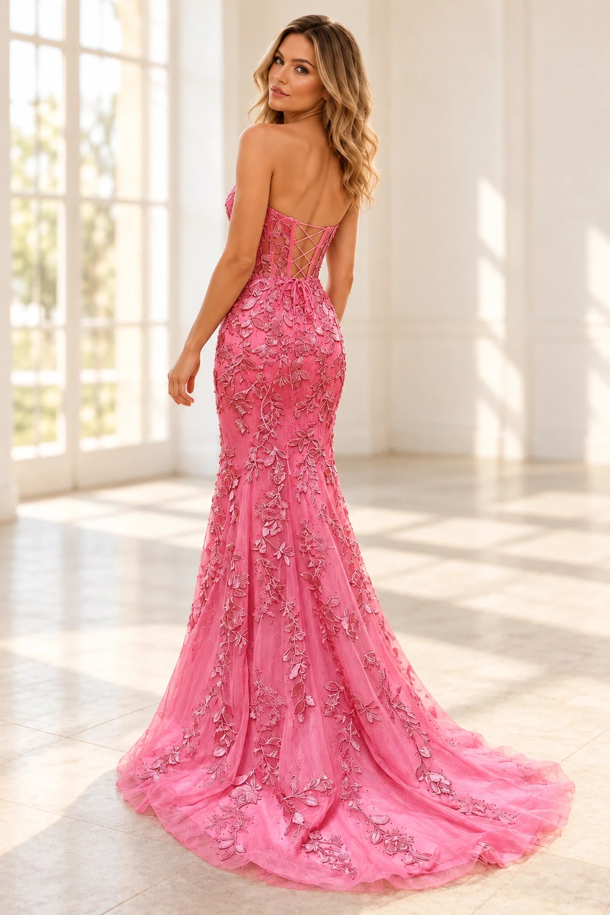 Back view of pink mermaid prom dress featuring an adjustable lace-up corset, floral lace appliqués and a flowing tulle sweep train.