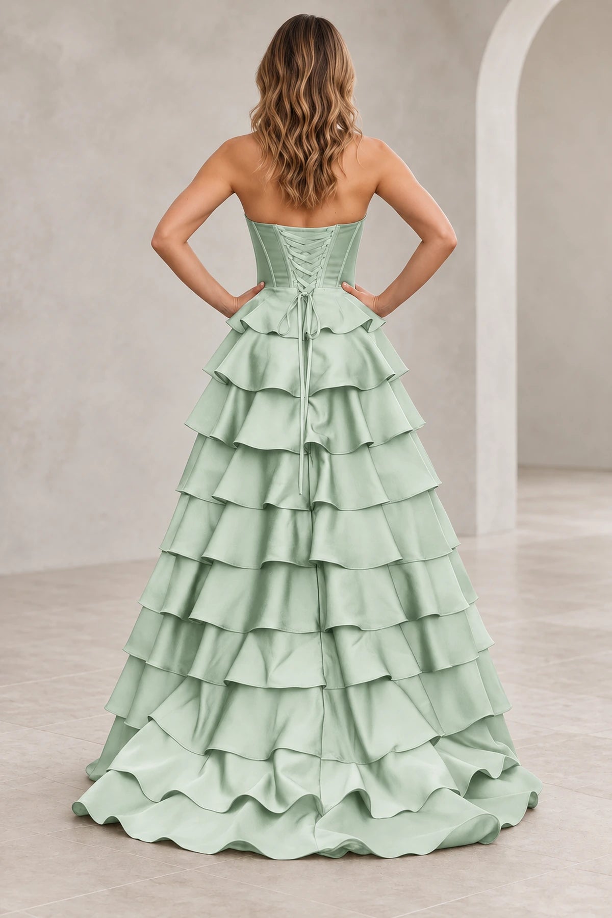 Back view of a mint green prom dress with matching corset lacing, a waist bow with long ties, and cascading ruffle tiers.