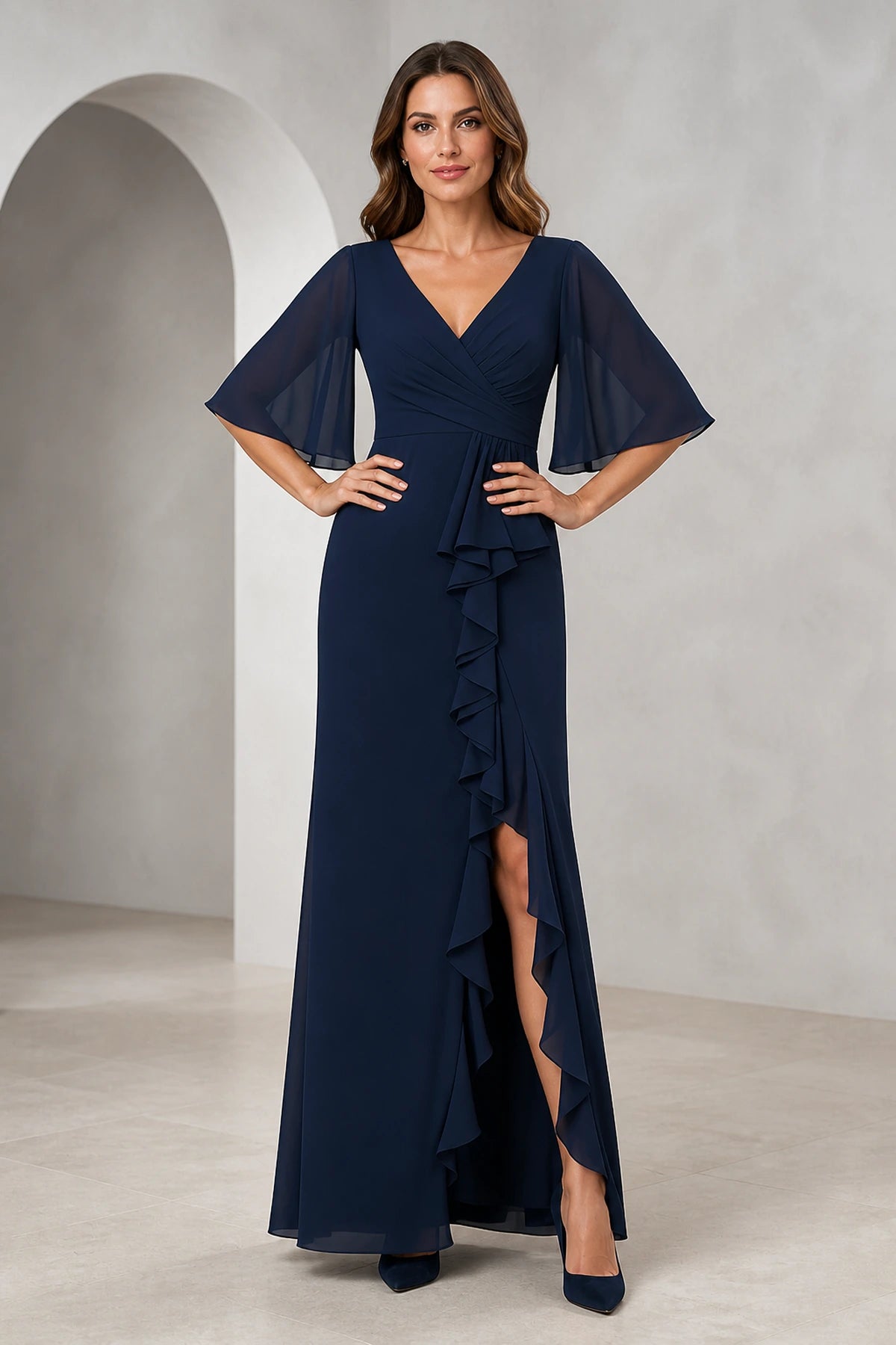 Front and back view of a navy mother of the bride dress with V-neck, sheer flutter sleeves, ruched bodice, cascading ruffle front slit, V-back, and floor-length silhouette