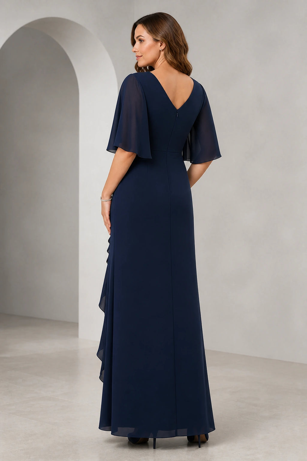 Front and back view of a navy mother of the bride dress with V-neck, sheer flutter sleeves, ruched bodice, cascading ruffle front slit, V-back, and floor-length silhouette