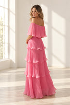 Back view of pink pleated chiffon wedding guest dress featuring off shoulder back, flutter sleeves, fitted waist and layered floor length skirt