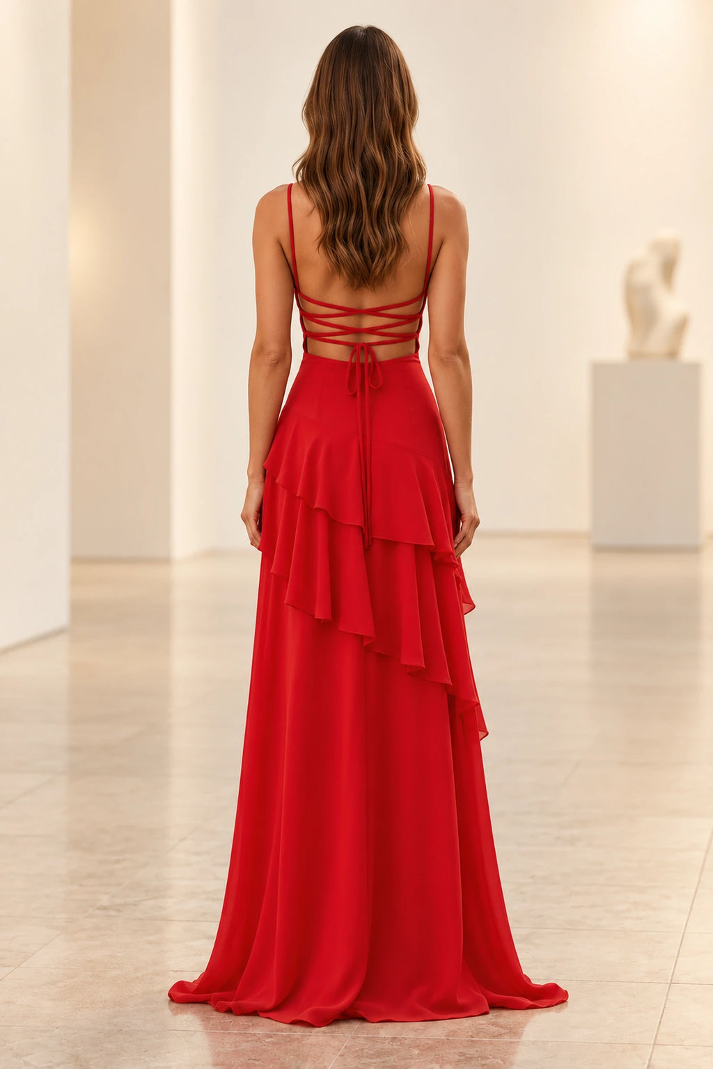 Back view of red chiffon prom dress with crisscross lace-up open back, spaghetti straps, flowing tie ribbons, and asymmetrical layered ruffle skirt.