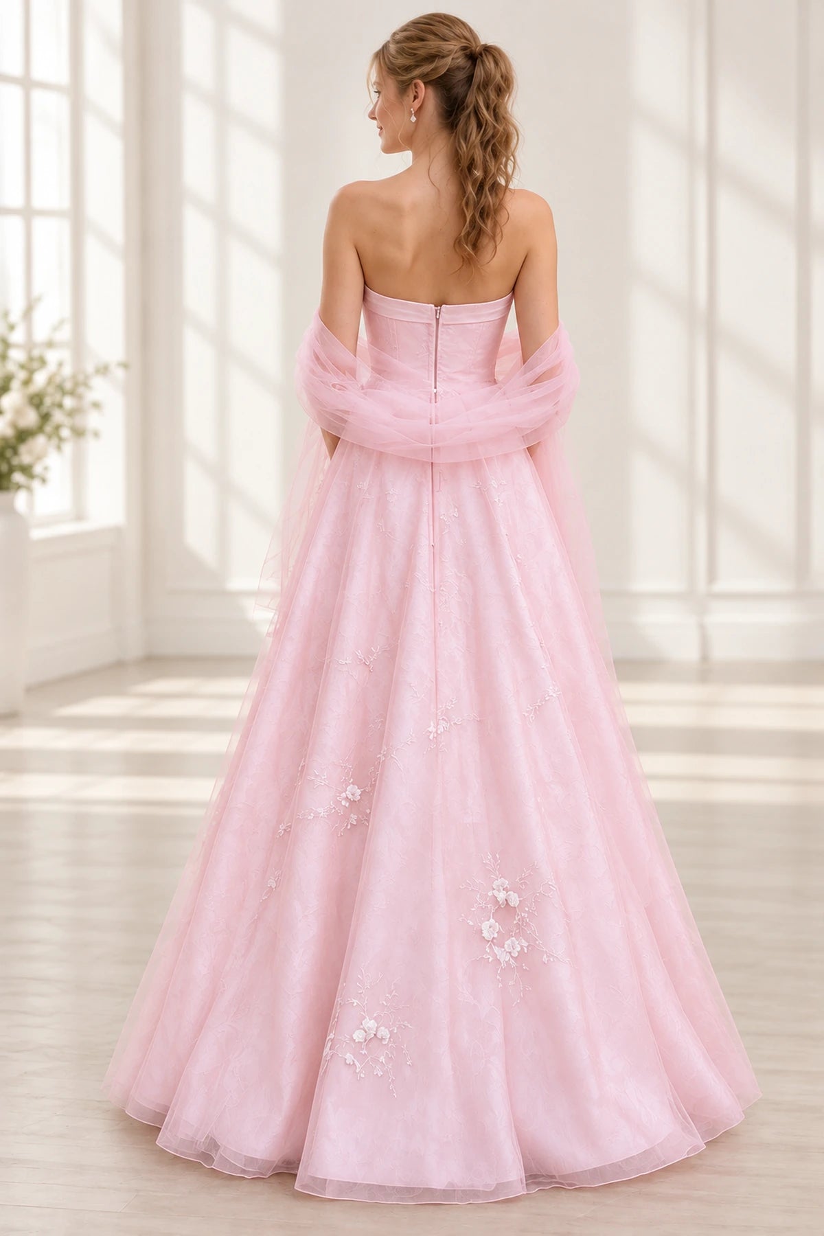 Blush pink tulle prom dress back view showing a strapless fitted bodice, center zipper, draped off-shoulder tulle wrap and floral embroidered A-line skirt